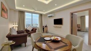 A modern hotel room with a dining area, a sofa set, a flat-screen TV, and a view of the cityscape. - Vaishnavi Beacon Hotel Patna (Patna)