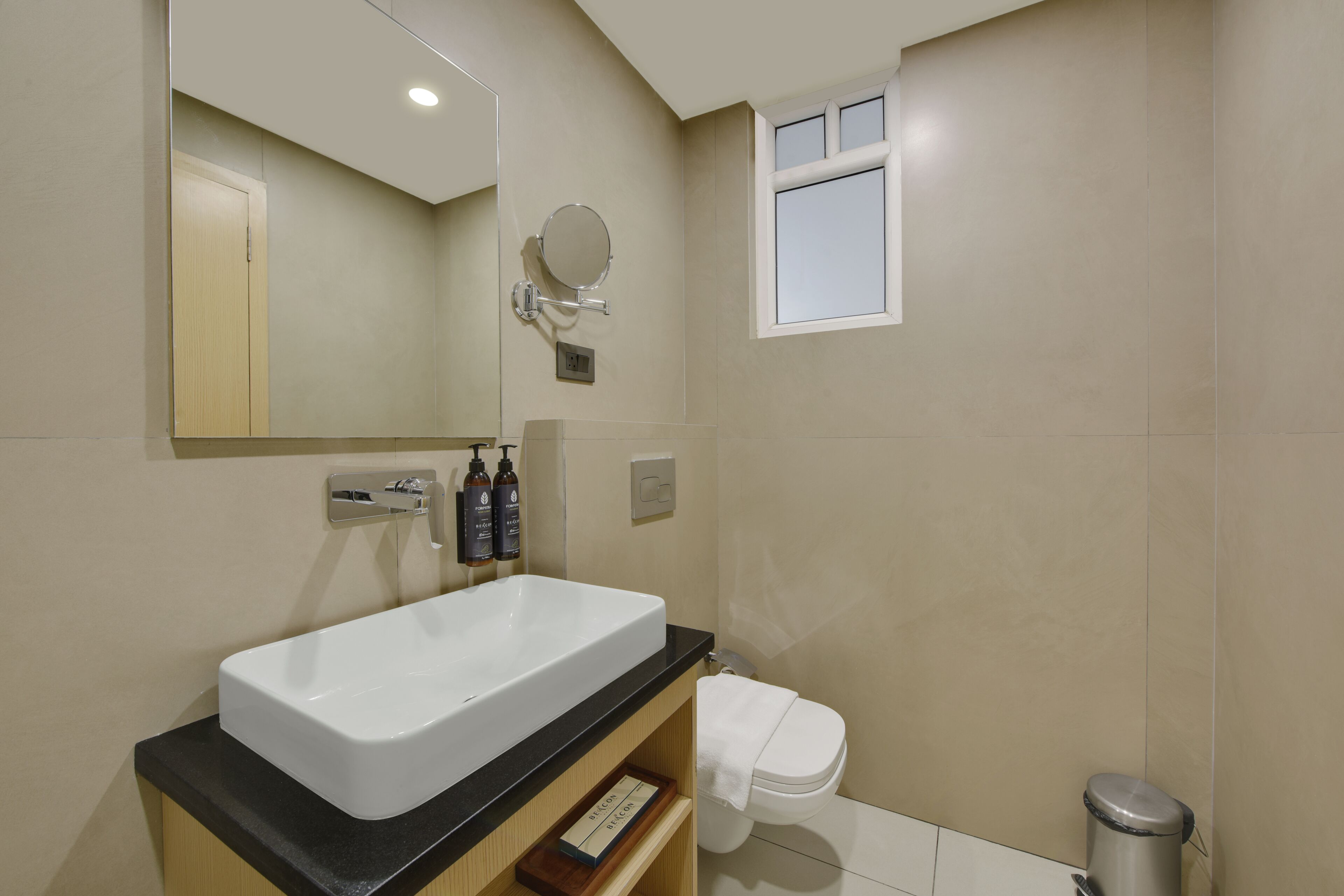 A modern bathroom with a large rectangular sink, a mirror, a small window, and a toilet.