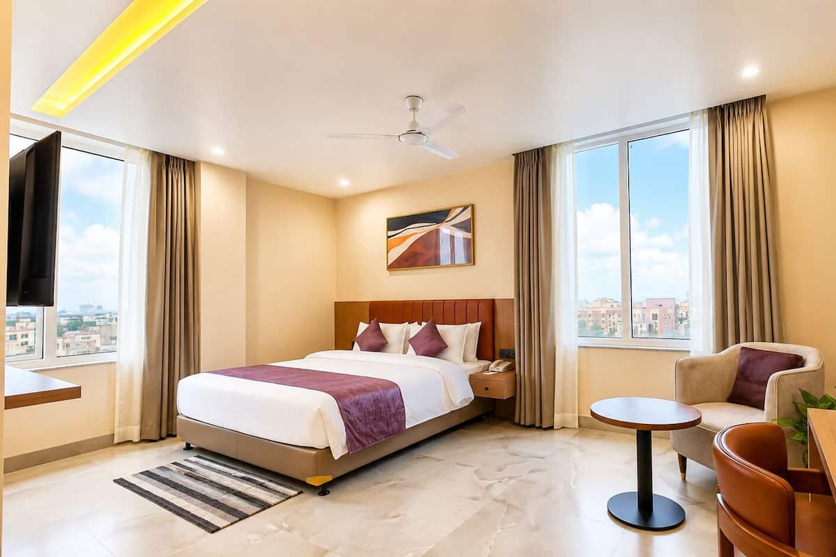 A hotel room with a bed, a sofa, a small table, a coffee station, and a view of the city.