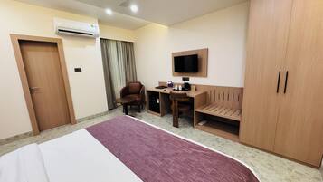 Una camera d'albergo con un letto, una scrivania, una sedia, televisione, armadio e condizionatore d'aria.