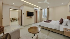 Habitación de hotel con cama, televisión, ventilador de techo, zona de comedor y vistas a la ciudad.