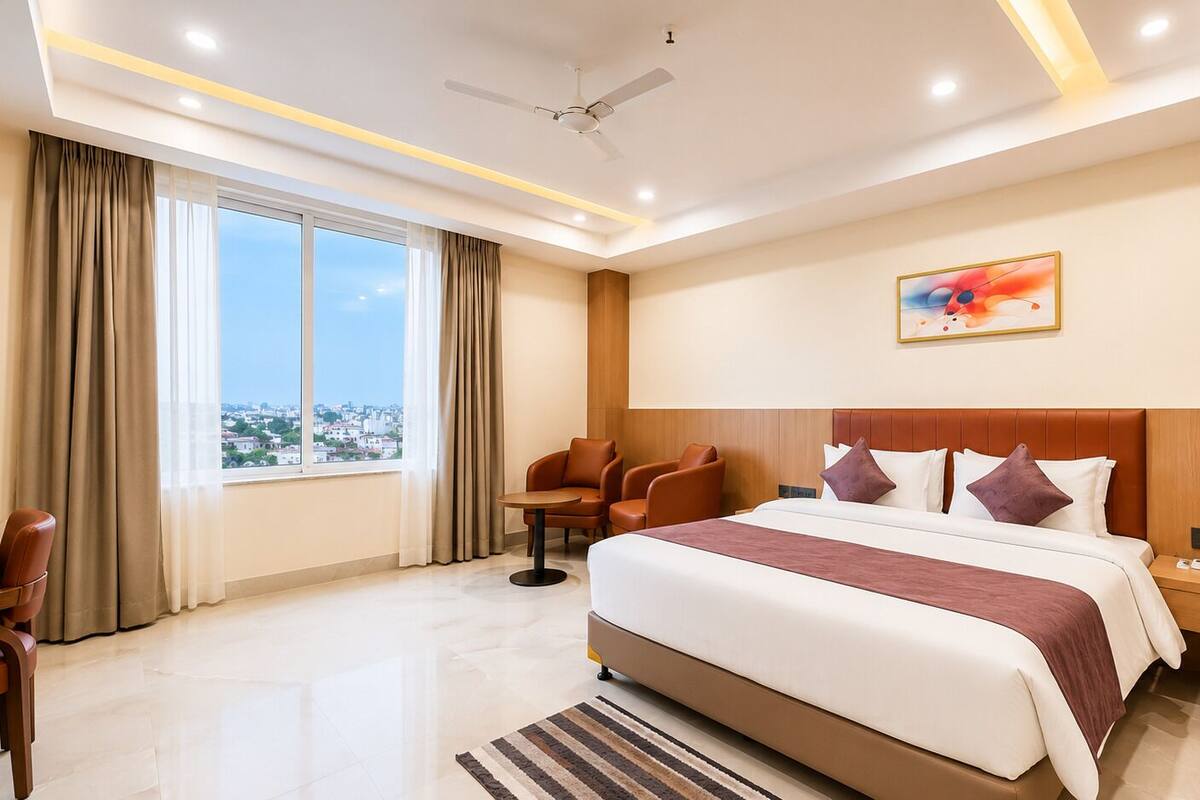 A hotel room with a large bed, a desk, a chair, a window with a city view, and a ceiling fan.