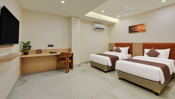 A hotel room with two beds, a desk, a chair, a television, an air conditioning unit, and a ceiling fan. - Vaishnavi Beacon Hotel Patna (Patna)