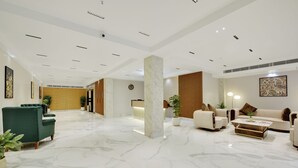 Un vestíbulo amplio con piso de mármol, área de descanso con sofás y sillones, y una mesa de recepción.