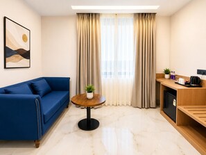 A modern hotel room with a blue sofa, a round wooden table, a small potted plant, and a kitchenette area. - Vaishnavi Beacon Hotel Patna (Patna)