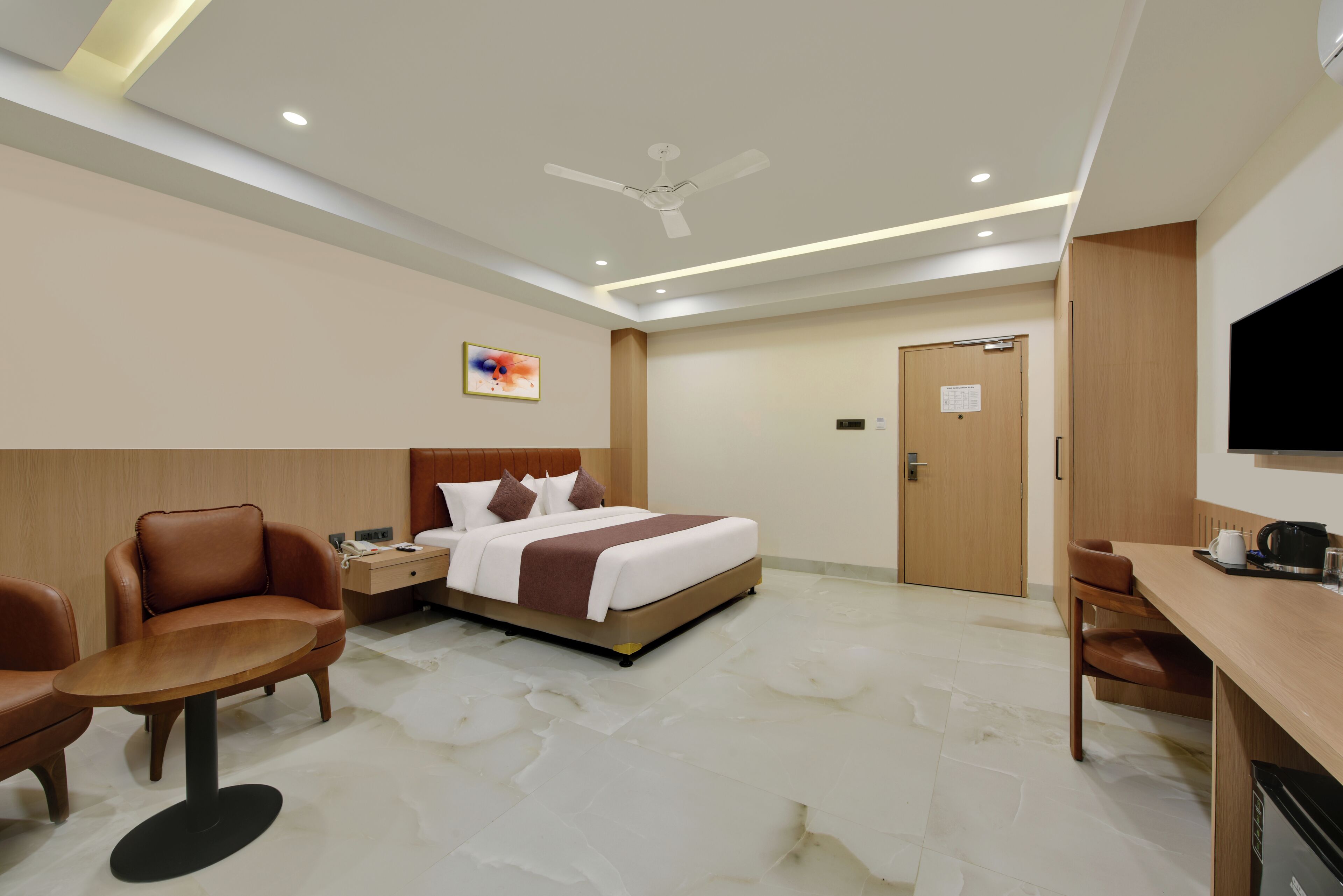 A hotel room with a bed, a desk, a chair, a television, and a ceiling fan.