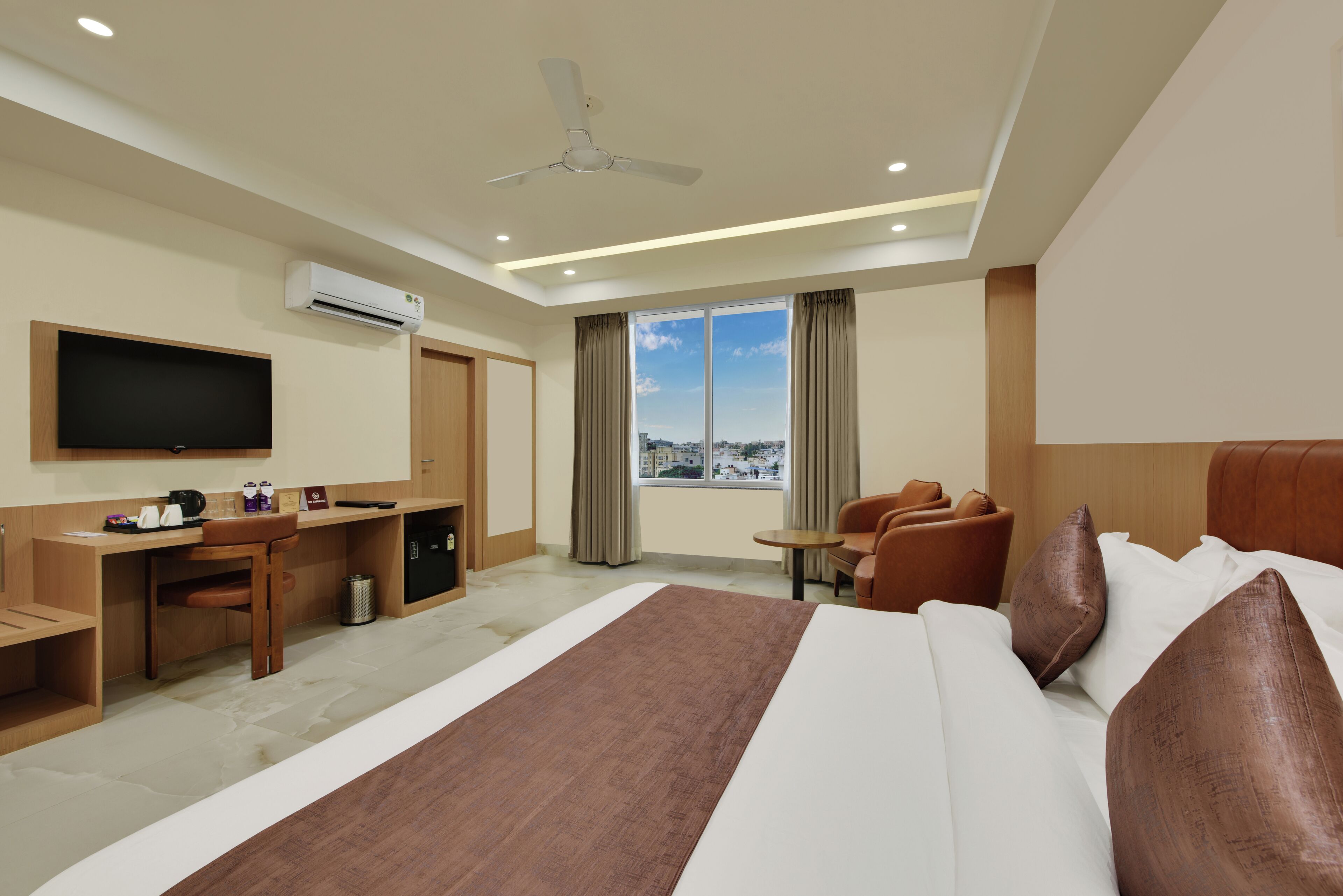 A hotel room with a bed, a desk, a chair, a television, and a window with a city view.