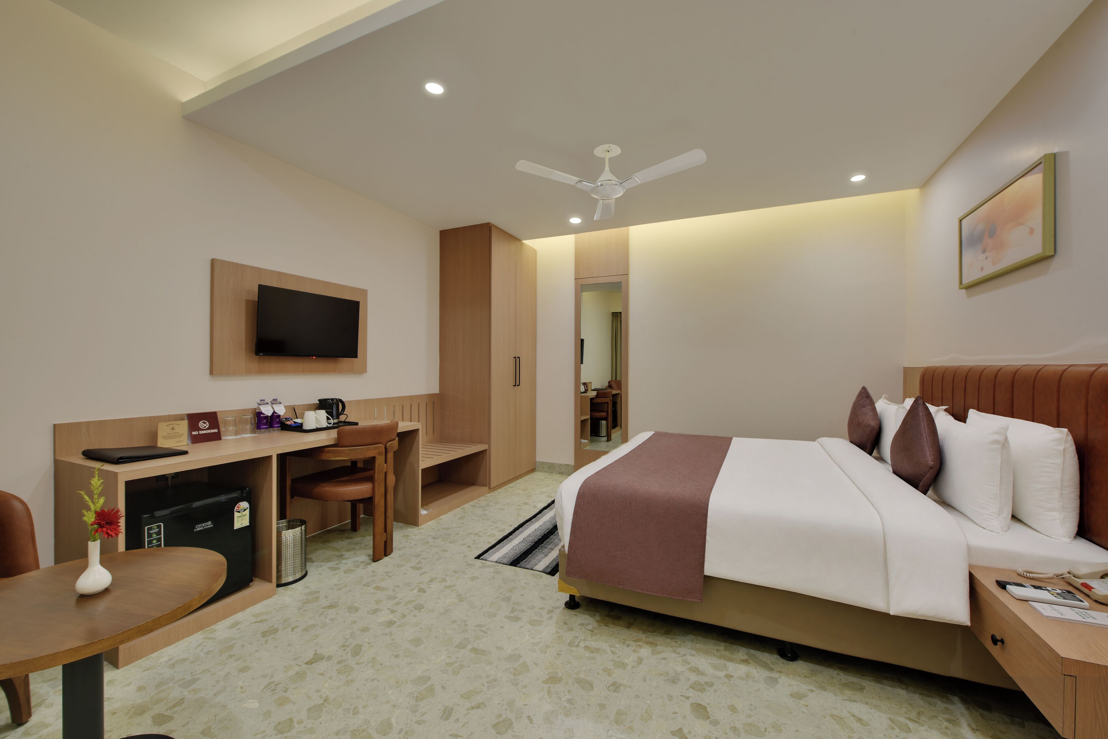 Habitación de hotel con cama, escritorio, silla y televisor en la pared.