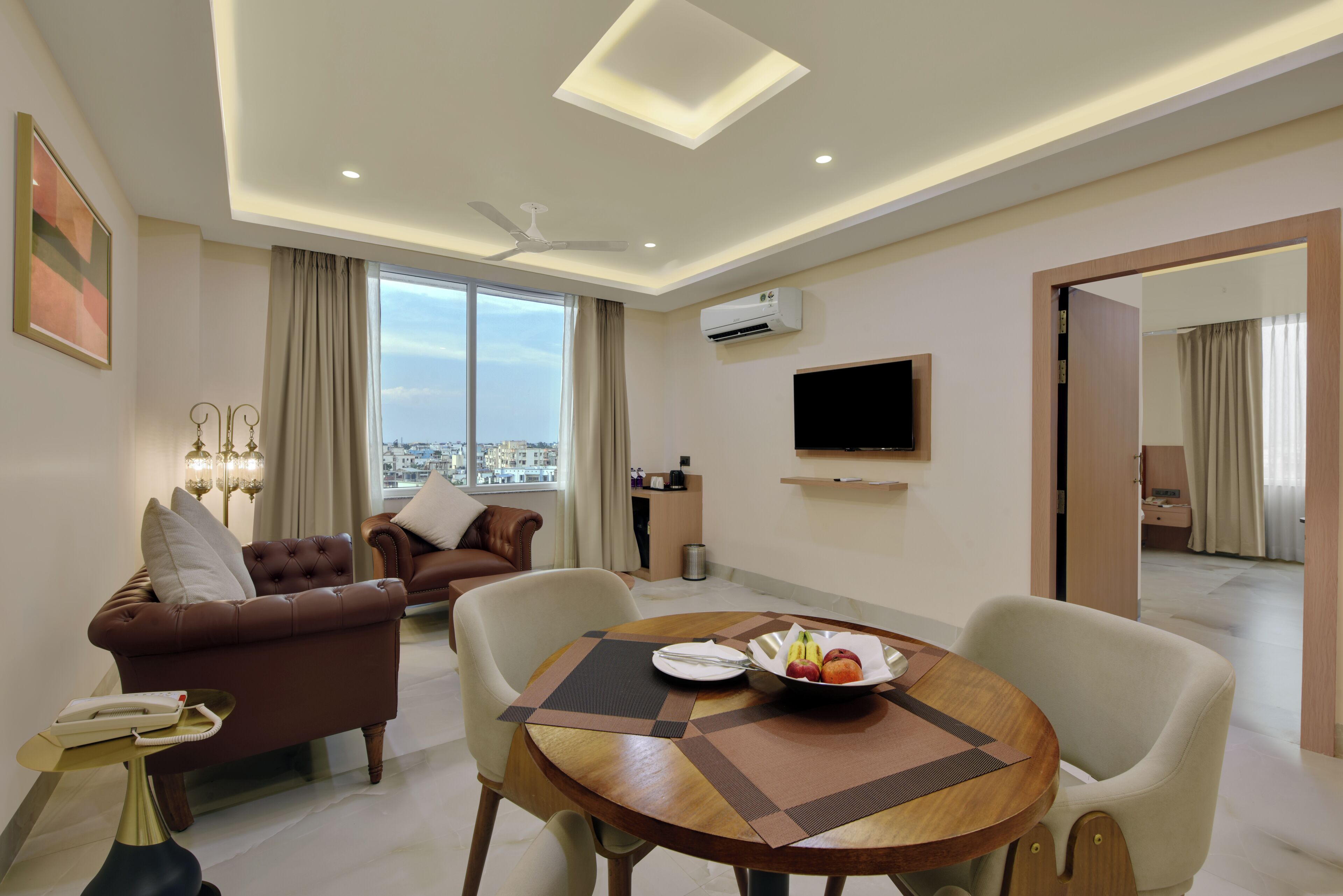 Habitación de hotel moderna con zona de comedor, sofá, televisión y vistas a la ciudad.