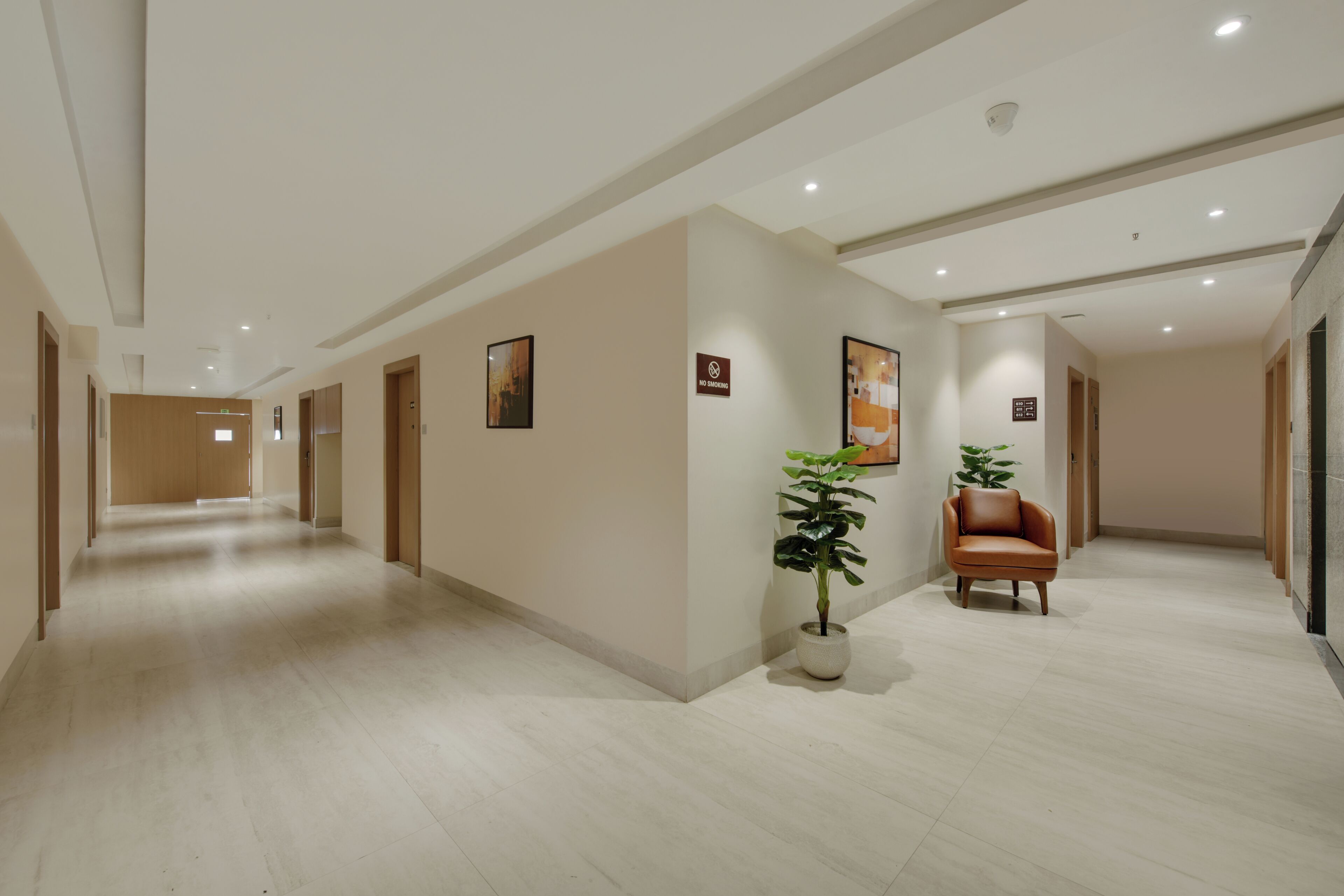 A hotel corridor with a no-smoking sign, a potted plant, and a leather chair.