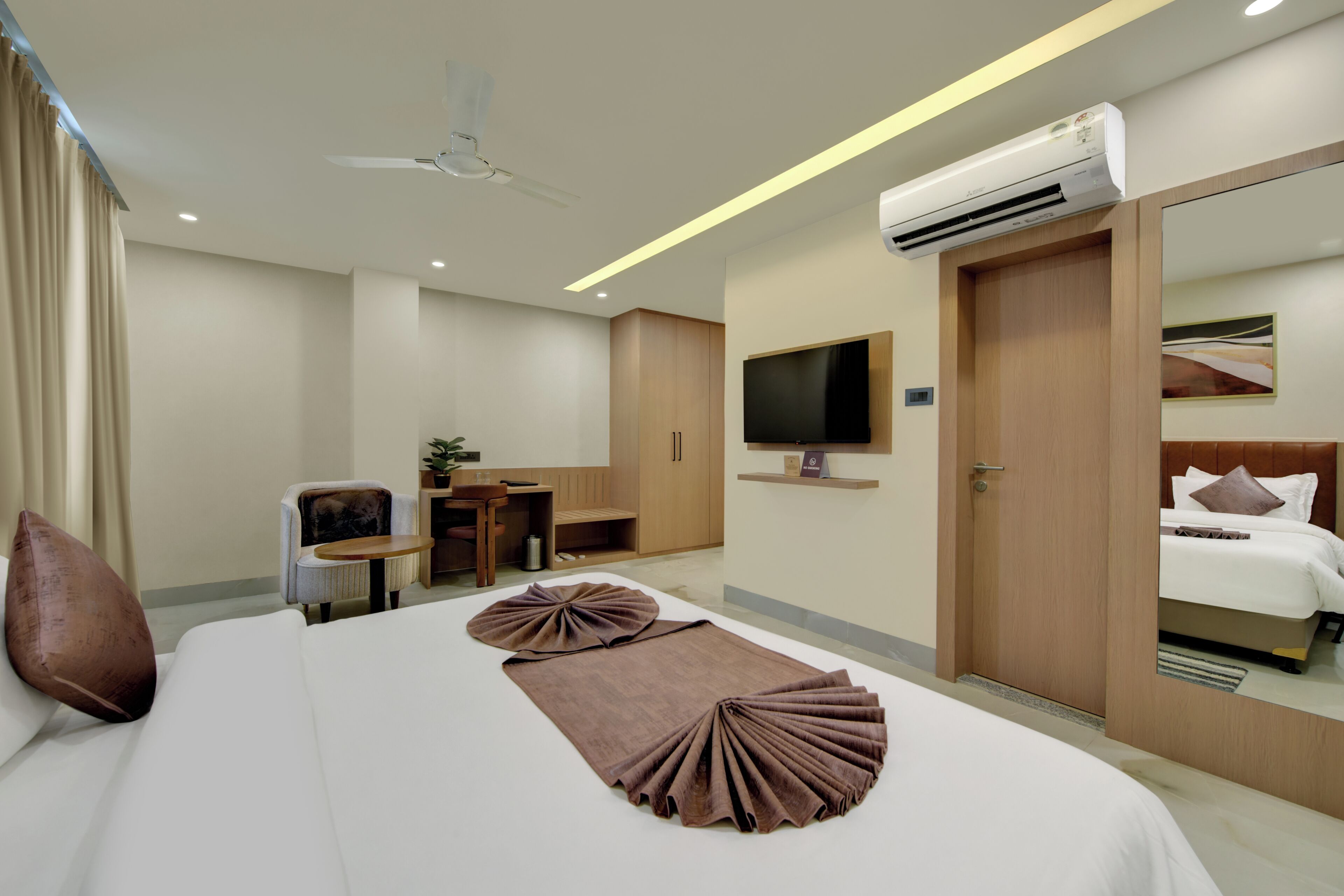 A hotel room with a bed, a desk, a chair, a television, and an air conditioning unit.