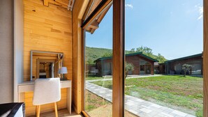 Habitación moderna con paredes de madera, un escritorio, una silla y un ventanal que ofrece vistas a un patio con edificios.