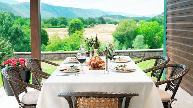 Mesa preparada para una comida con vistas a un viñedo y montañas.