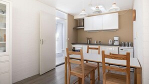A compact kitchen with white cabinets, a dining table with wooden chairs, and pendant lights. - Buitenplaats Herkingen 25-A (Herkingen)