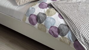 A bed with a patterned bedspread and pillows, a textured throw blanket, and a white brick wall. - Buitenplaats Herkingen 25-A (Herkingen)