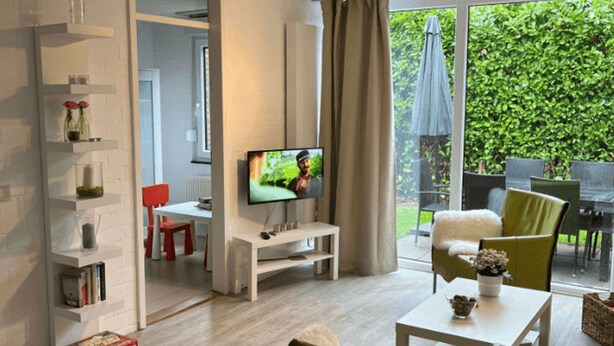 A modern living room with a TV, green chairs, a white table, and a bookshelf. - Buitenplaats Herkingen 25-A (Herkingen)