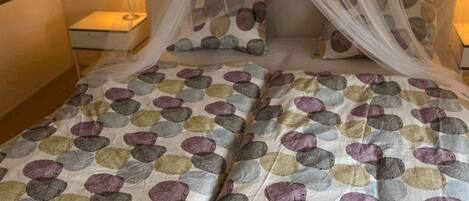A bed with a canopy, pillows with a pebble pattern, a bedside lamp, and a wooden floor.