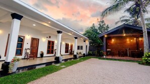 A building with a covered porch, outdoor seating, and a brick structure with lights. - Sand & Sea Villa  (Negombo)