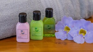 Three bottles of liquid on a wooden surface with a towel and a flower. - Sand & Sea Villa  (Negombo)