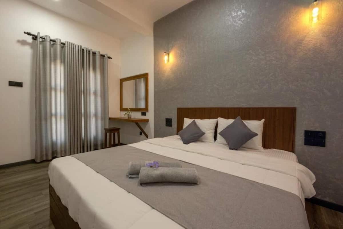Habitación de hotel con una cama grande, cabecera de madera, espejo y lámpara fijada a la pared.