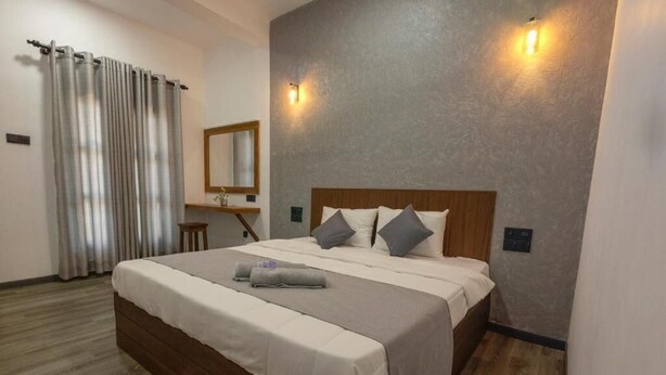 A bedroom with a wooden bed, grey bedding, a mirror, and two wall-mounted lights. - Sand & Sea Villa  (Negombo)