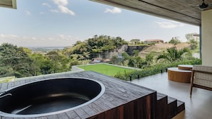 A modern outdoor bathroom with a large bathtub, wooden steps, and a view of a lush landscape. - KONO Villas & Resort (Kutuh)