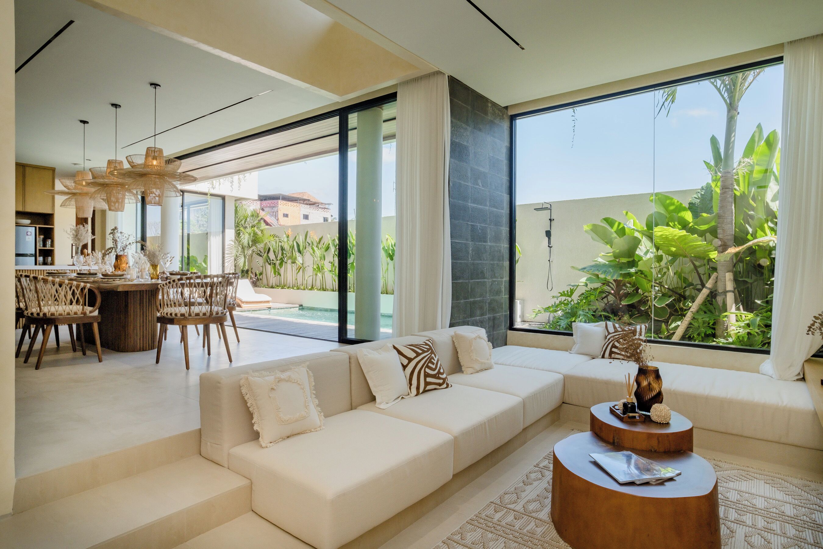 A modern living room with a sofa, dining area, and large windows overlooking a garden.