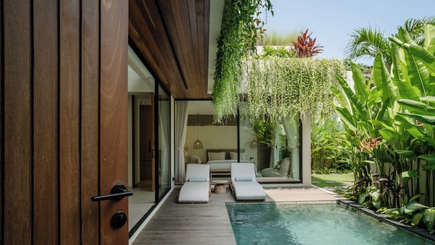 A poolside area with lounge chairs, a wooden deck, and a hanging garden. - KONO Villas & Resort (Kutuh)