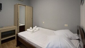 Ein Einzelbett mit weißer Bettwäsche, ein Holzschrank, ein kleiner Nachttisch und ein an der Wand befestigtes Fernsehgerät.