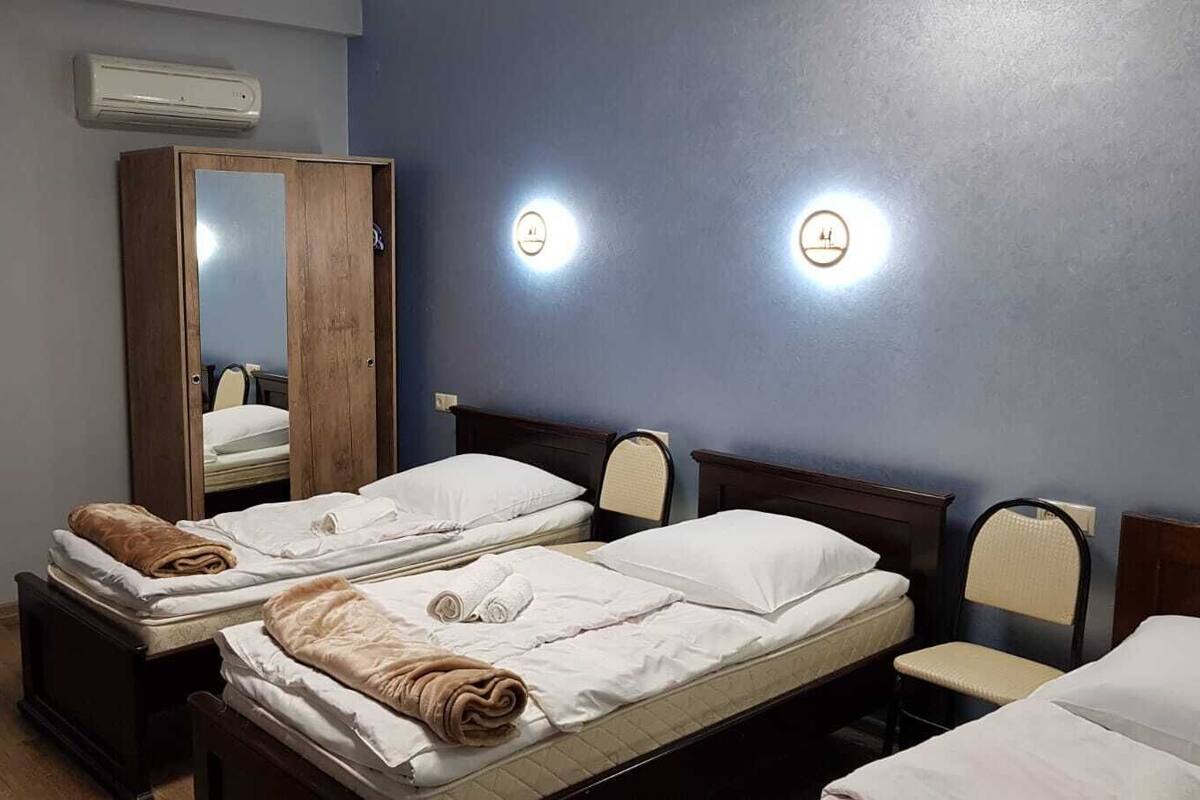 Une chambre d’hôtel avec deux lits, une armoire en bois, un miroir et deux lampes fixées au mur.