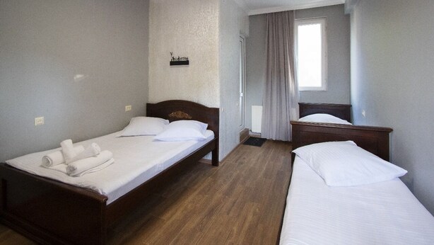 Ein Hotelzimmer mit zwei Einzelbetten, einem Fenster mit Vorhängen, einer kleinen Wanddekoration und einem Holzboden.