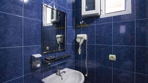 Ein Badezimmer mit einem weißen Waschbecken, einem Spiegel und einem an der Wand befestigten Föhn.