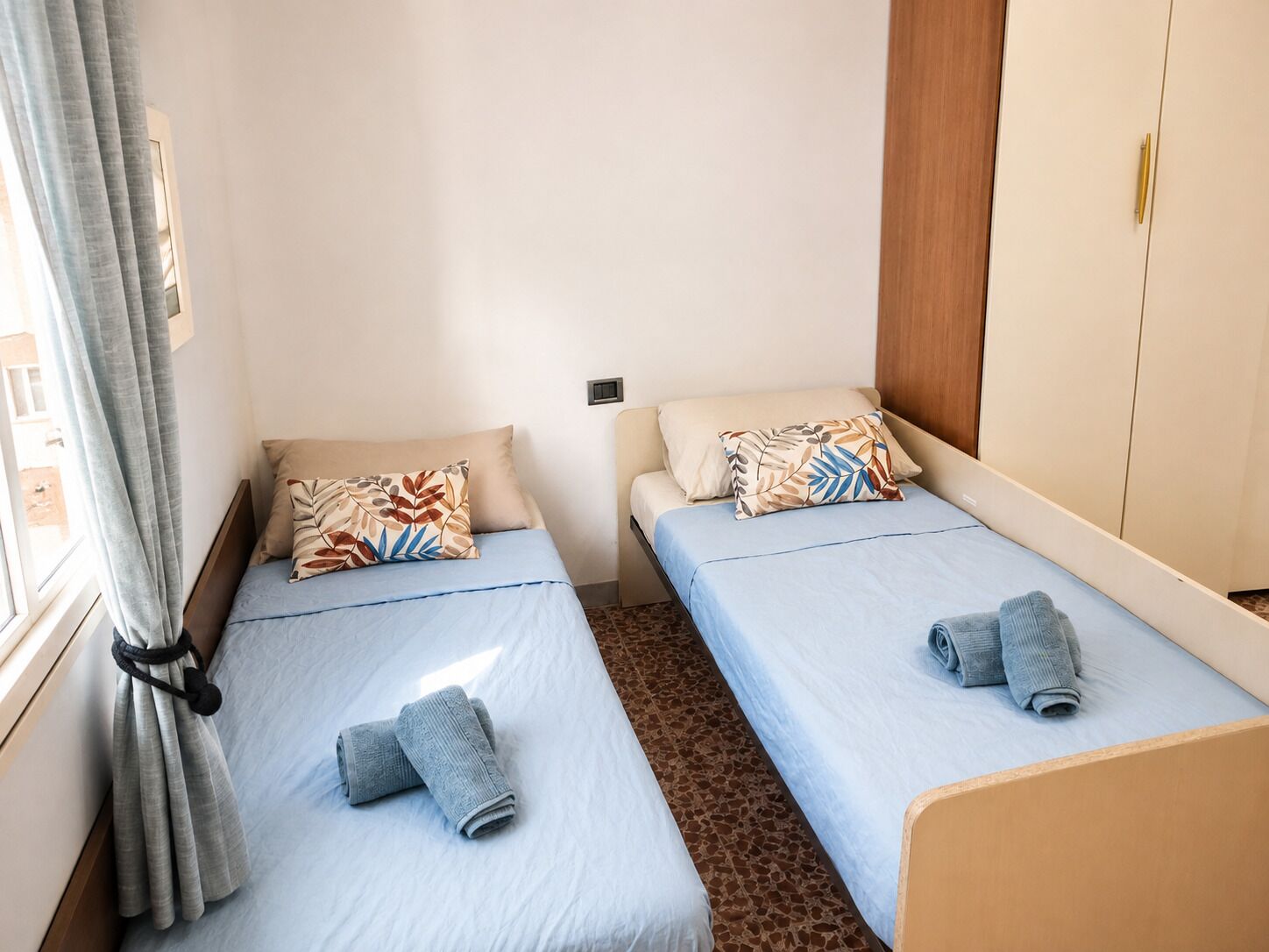 Une petite chambre compacte avec deux lits simples, chacun étant équipé d’un oreiller et d’une serviette roulée.