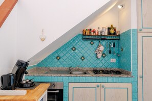 Een keuken met een blauwe tegelachtergrond, een koffiezetapparaat, een spoelbak en een fornuis.