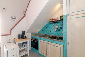 A compact kitchen with a gas stove, a coffee maker, and a shelf with various items. - Apartment 'Sole-mare' with Sea View, Wi-Fi and Air Conditioning (Porto Ottiolu)