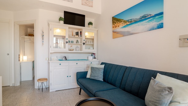 A living room with a blue sofa, a white cabinet with shelves, a flat-screen TV, and a painting of a beach scene. - Apartment 'Sole-mare' with Sea View, Wi-Fi and Air Conditioning (Porto Ottiolu)
