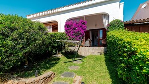 A white building with a tiled roof, a stone pathway leading to the entrance, and a well-maintained garden with hedges and a tree. - Apartment 'Sole-mare' with Sea View, Wi-Fi and Air Conditioning (Porto Ottiolu)
