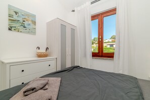 A bedroom with a bed, a dresser, a painting, and a window with a view. - Apartment 'Sole-mare' with Sea View, Wi-Fi and Air Conditioning (Porto Ottiolu)