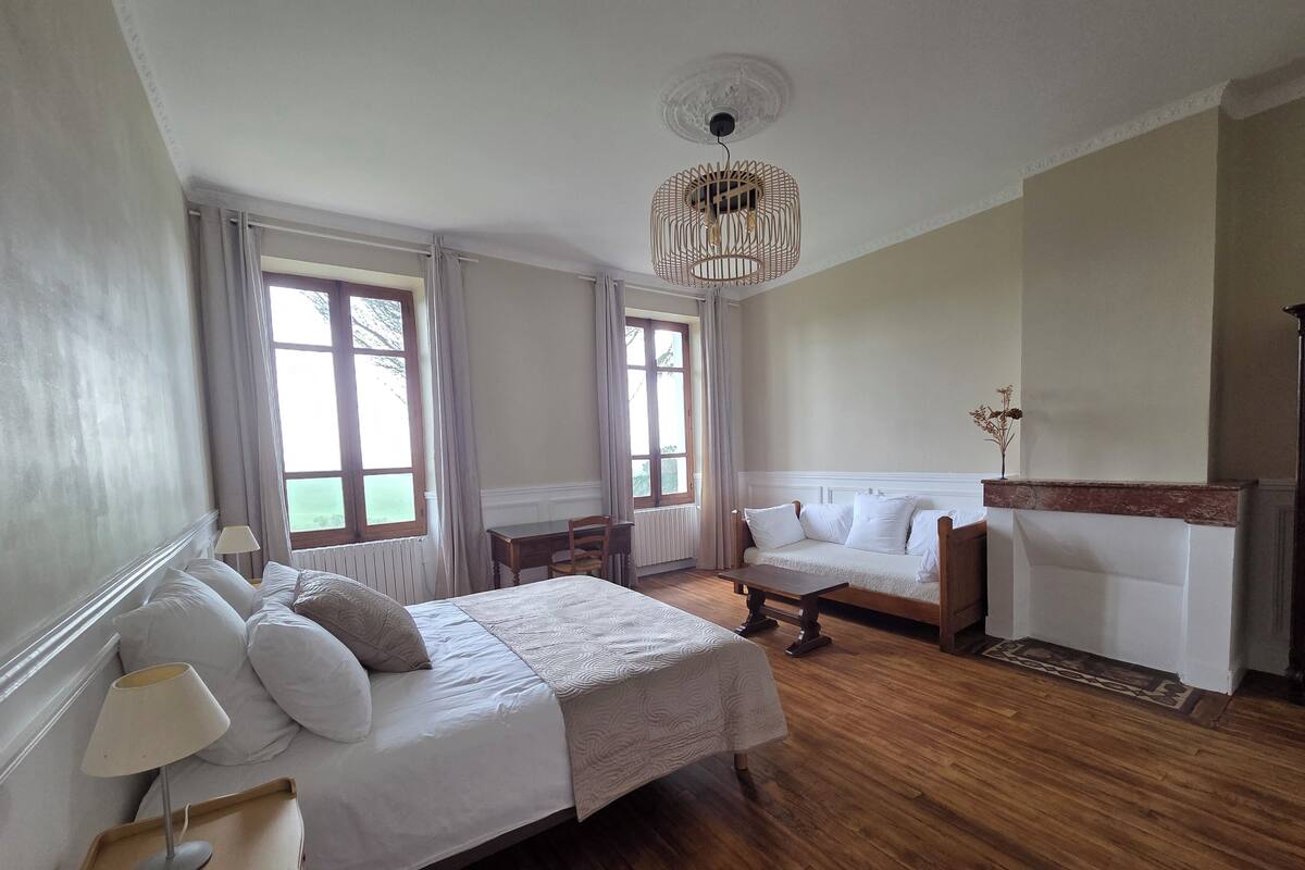 A bedroom with a bed, bedside table, lamp, wooden floor, and a hanging light fixture.