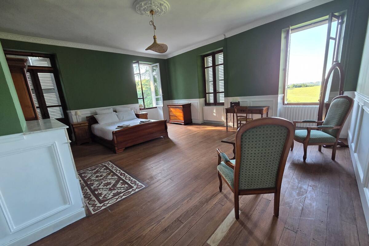 A room with a bed, a chair, a table, and a fireplace.