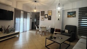A modern living room with a flat-screen TV, a dining area with a table and chairs, a sofa, and a coffee table. - Bright & Elegant Apartment - Comfort & Style in Piraeus (Pireas)