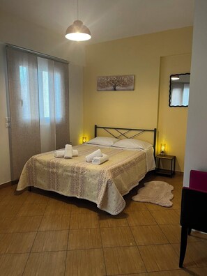 A bedroom with a bed, bedside lamps, a painting, a mirror, and a door. - Bright & Elegant Apartment - Comfort & Style in Piraeus (Pireas)