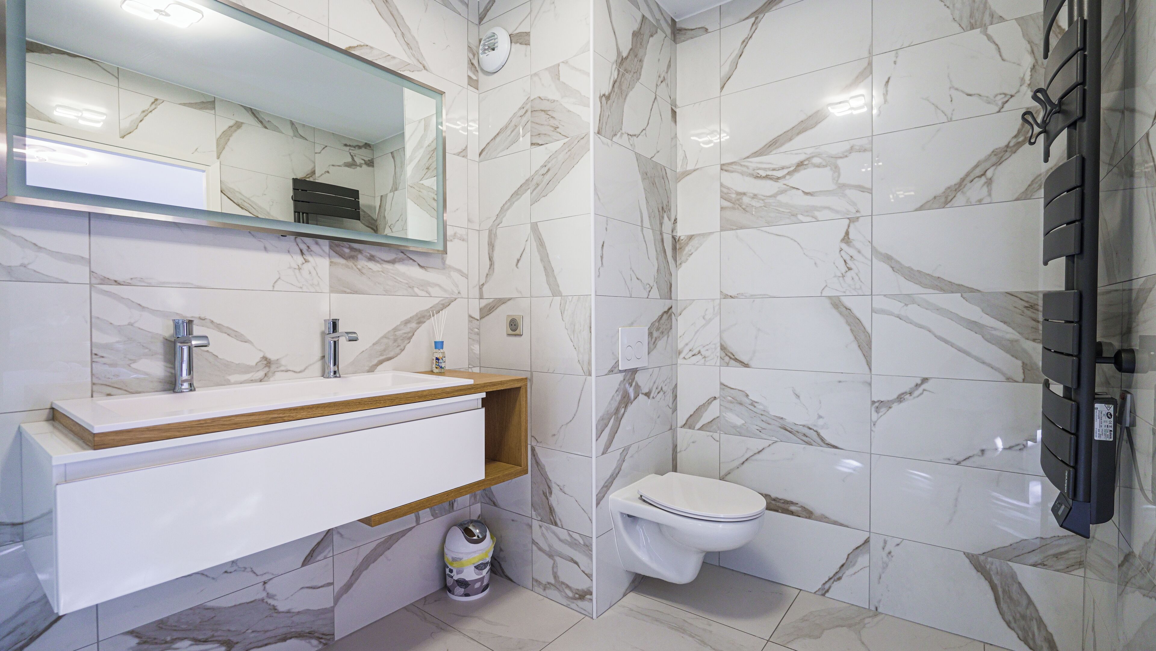 A bathroom with a marble-tiled wall, a sink with a wooden countertop, a toilet, and a mirror above the sink.