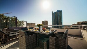 Une terrasse sur le toit, aménagée avec des meubles en osier, une table dressée pour le dîner et une vue sur les gratte-ciel.