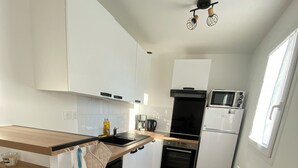 A modern kitchen with white cabinets, a wooden countertop, a dishwasher, an oven, a microwave, and a built-in refrigerator. - House for rent Audierne (Audierne)