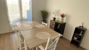 A dining area with a wooden table, white chairs, a potted plant, and a small cabinet with decorative items. - House for rent Audierne (Audierne)