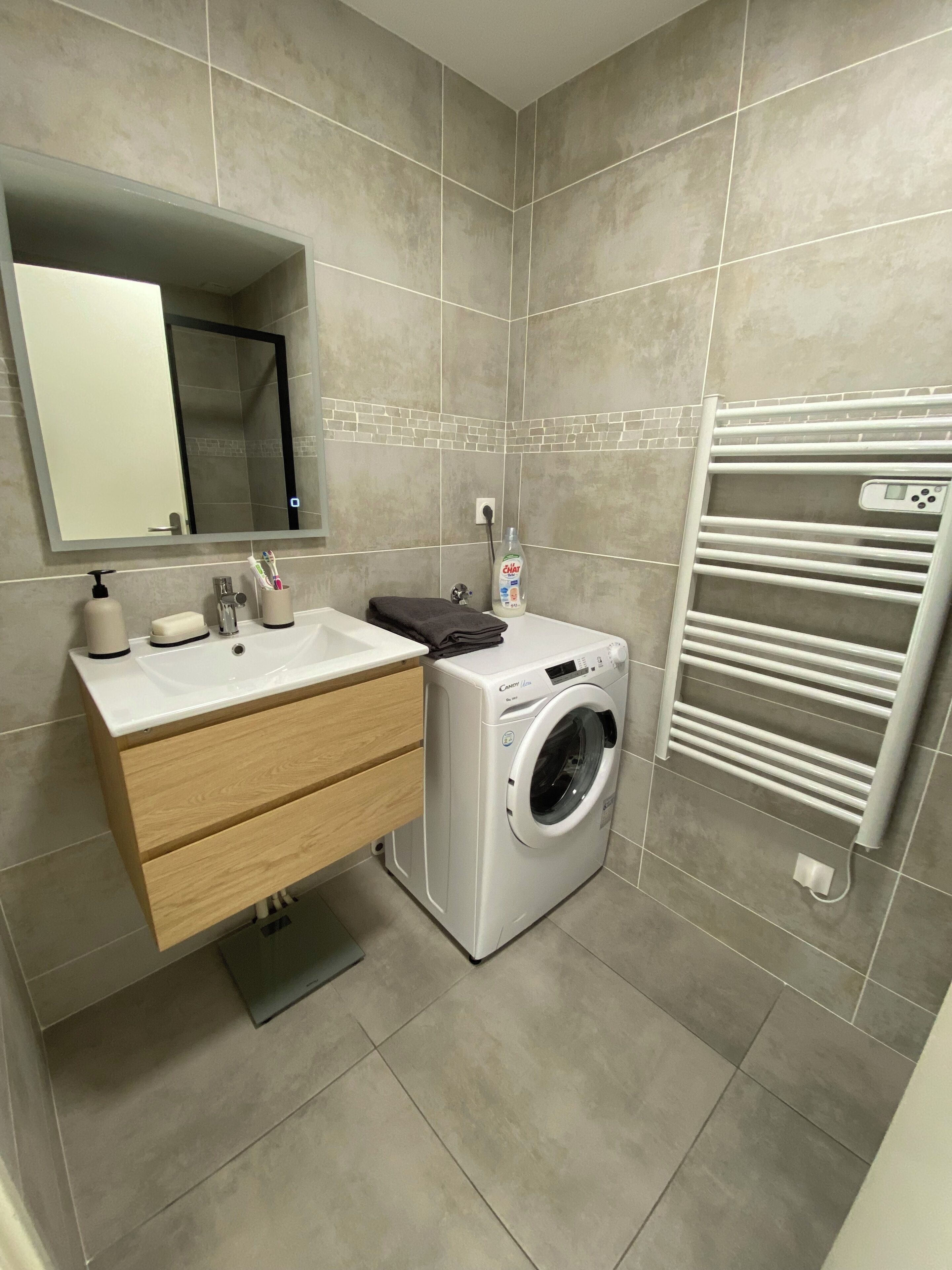 A modern bathroom with a sink, mirror, and a built-in washing machine.