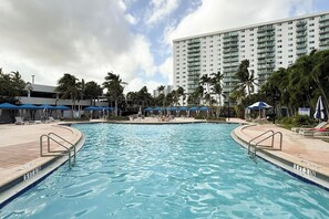 Ein Swimmingpool mit Tiefenmarkierung von 1,60 Metern, umgeben von Liegestühlen und Sonnenschirmen, mit einem hohen Gebäude im Hintergrund.