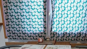 A round wooden table with two metal chairs, a candle, and a window with floral curtains. - Agnès's garden caravan 37150 (Luzillé)
