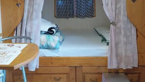 A bedroom with a canopy bed, a window with patterned curtains, a bedside table, and a small bedside cabinet. - Agnès's garden caravan 37150 (Luzillé)